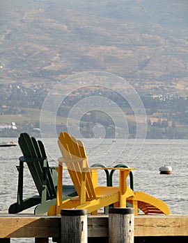 Two wooden armchairs on a pier facing Okanagan Lake.