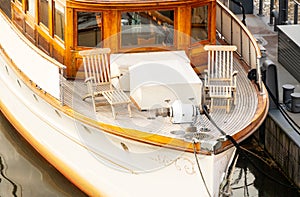 Two wooden armchairs stand on the front deck of a small moored ship