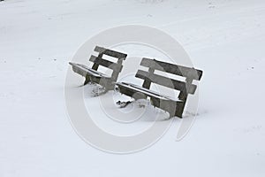 Two wooden benches covered with snow during a blizzard