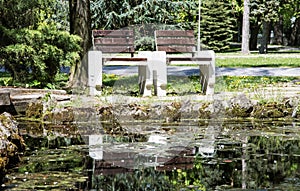 Two wooden benches reflecting in water in the park