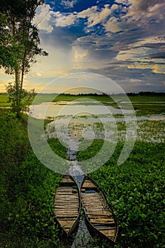 two wooden boats docked on the shore of a lake at sunset