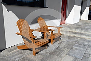 Two wooden chairs connected by a small table standing in front of a house.