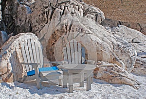 Two wooden chairs and small table at crystal sand of white marble, Greece