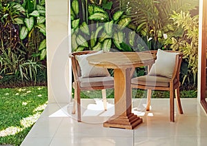 Two wooden chairs and table in the garden full of green tropic plants