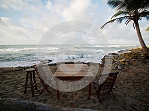 Two wooden chairs and table on the ocean beach at sunset.