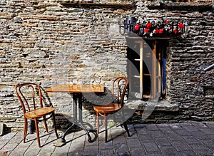 Two wooden chairs and table by a stone-built wall