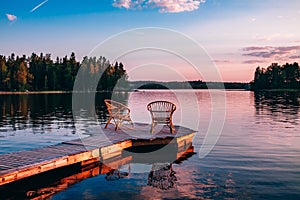 Two wooden chairs on a wood pier overlooking a lake at sunset