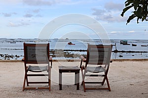 Two wooden chairs and wooden table on sand beach with blurred blue sky over sea view