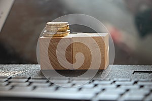 Two Wooden cubes with the pile of coins on computer keyboard. ,Tax or online business profit Concept. Selective focus