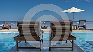 Two wooden deck chairs with soft mattresses stand by the swimming pool.