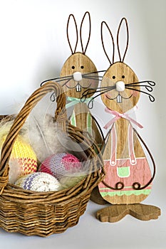 Two wooden Easter bunnies near a wicker basket with three crocheted eggs in front of a bright background