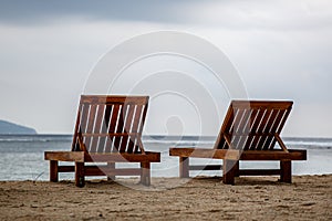 Two wooden empty deck chairs on the beach. Overcast