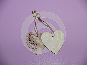 Two wooden hearts on a string on a pink textured background.