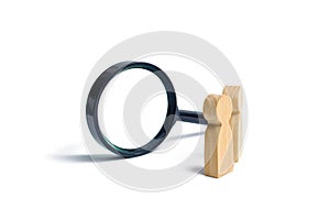 Two wooden human figure stands near a magnifying glass on a white background. The concept of the search for people and workers.