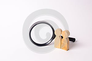 Two wooden human figure stands near a magnifying glass on a white background. The concept of the search for people and workers.