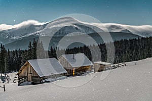 Two wooden log cabins under moonlight in winter Carpathian mountains