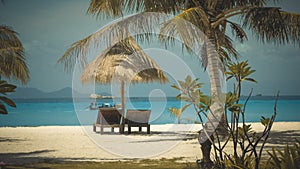 Two wooden lounge chairs under palm tent on beach