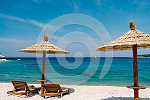 Two wooden loungers on the white sand, on a paradise beach near the town of Primosten in Croatia. Straw beach umbrella