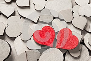 Two wooden painted red hearts among many colorless wooden hearts