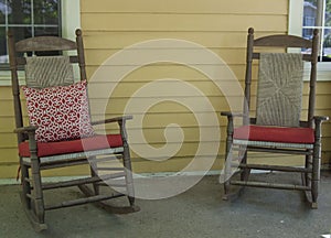 Two wooden rocking chairs with red cushions on a farmhouse porch