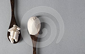 Two wooden spoons with collagen powder and protein capsules on a light blue background, healthy and anti-aging concept