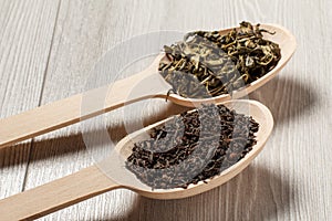 Two wooden spoons with dry leaves of black and green tea