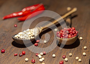 Two wooden spoons with red and white pepper on a wooden surface
