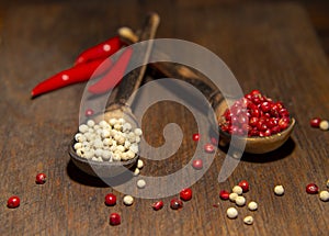 Two wooden spoons with red and white pepper on a wooden surface