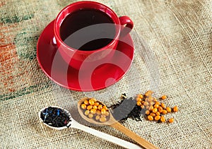 Two wooden spoons with vitaminic healthy sea buckthorn berries and black tea over sackcloth background.