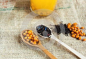 Two wooden spoons with vitaminic healthy sea buckthorn berries and black tea over sackcloth background. cooking,