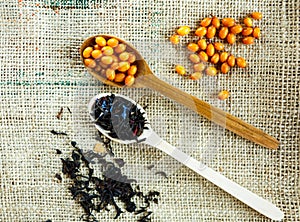 Two wooden spoons with vitaminic healthy sea buckthorn berries and black tea over sackcloth background. cooking,