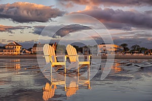 Two wooden traditional armchairs on a sandy beach at sunrise overlooking the coastline. Atlantic Ocean. USA. Maine.