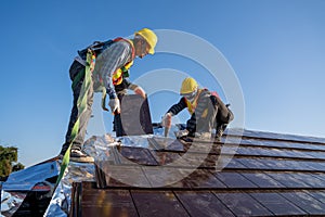 Two work construction worker wearing safety height equipment harness belt during working and install new ceramic tile roof with