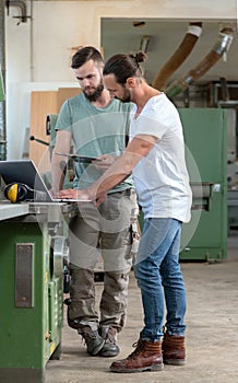 Two worker in a carpenter`s workshop with computer and clipboard
