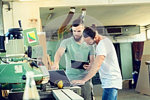 Two worker in a carpenter`s workshop with computer and clipboard