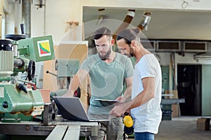 Two worker in a carpenter`s workshop with computer and clipboard