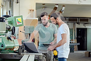 Two worker in a carpenter`s workshop with computer and clipboard