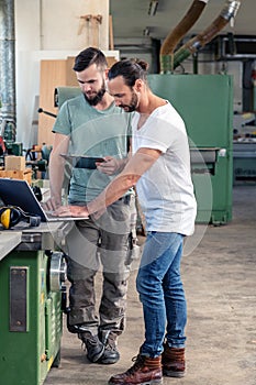 Two worker in a carpenter`s workshop with computer and clipboard