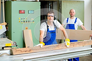 Two worker in workshop using saw machine