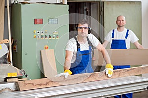 Two worker in workshop using saw machine