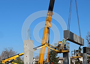 Two workers on two cherry pickers install a prefab concrete slab, lifted by a telescopic crane, on the new wall of the building u photo