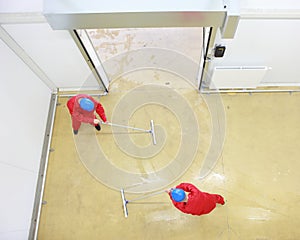 Two workers cleaning floor in industrial building