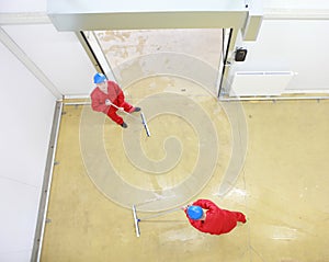 Two workers cleaning floor in industrial building