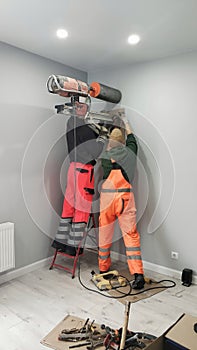 Two workers drill a hole in wall, diamond drilling. Preparation for installation of Heat Exchangers - Recuperator photo