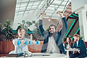 Two workers exercising with dumbbells in office.