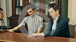 Two workers get berated by boss at office table with wood bookcase on background