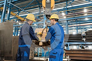 Two workers handling heavy loading lifted by crane