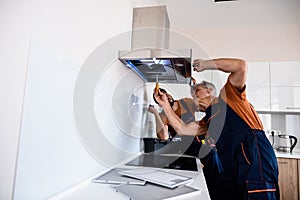 Two workers, handyman in uniform installing or repairing a kitchen extractor, replacing filter in cooker hood