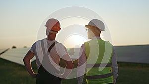 Two workers in helmets having conversation on solar station.
