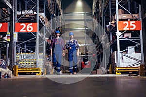 Two workers with helmets on heads walking in warehouse